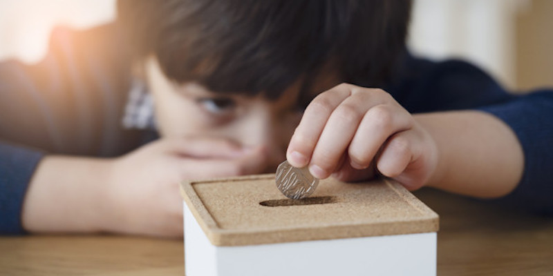 Blurry face of kid with thinking face putting 10 pence on money box, Selective focus little boy making stack British money coins and counting. Learning financial responsibility and saving for future